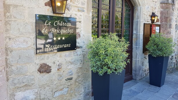 Een stenen gebouw met een bordje voor 'Le Chateau de Bricquebec Restaurant'.