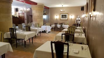 Een restaurant met meerdere tafels en stoelen, een stenen pilaar en een kroonluchter.