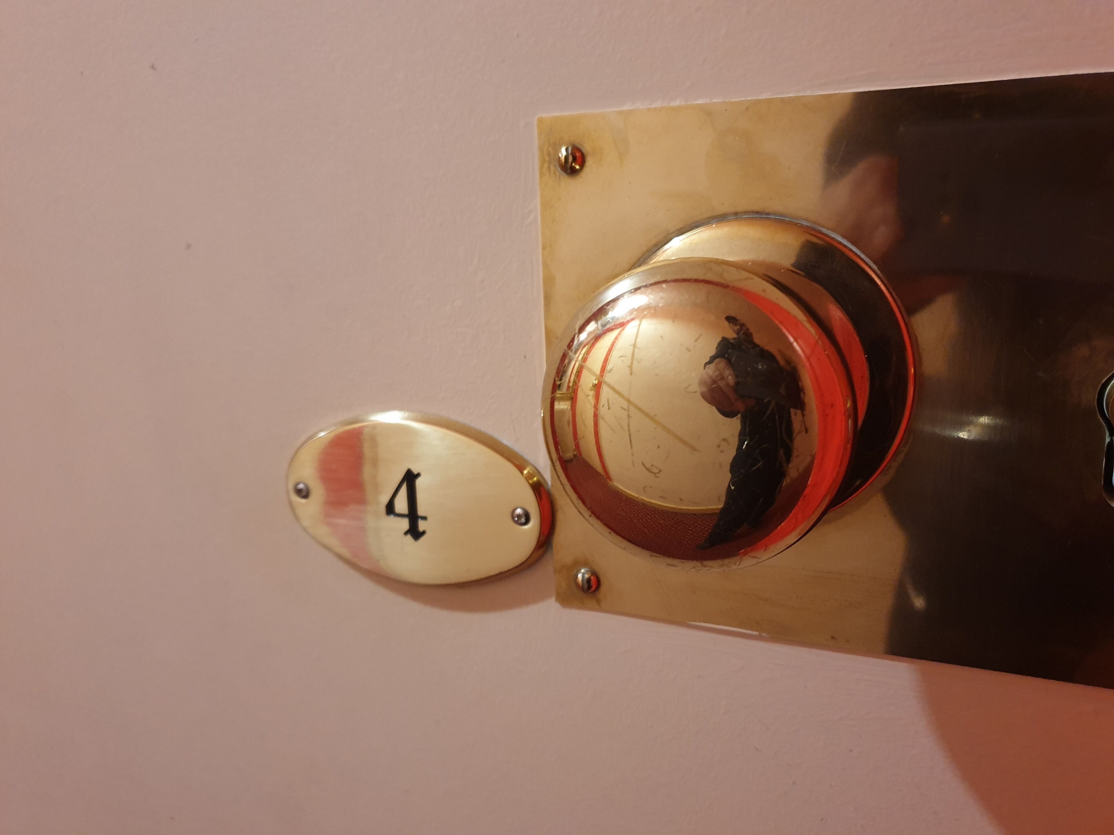 A brass doorbell with a glass panel reflecting a person, and a brass plaque with the number 4.