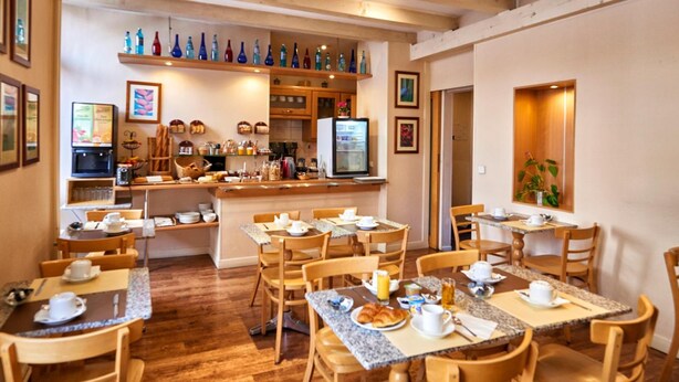 Un área de desayuno con mesas y sillas de madera, una máquina de café y una variedad de alimentos para el desayuno.