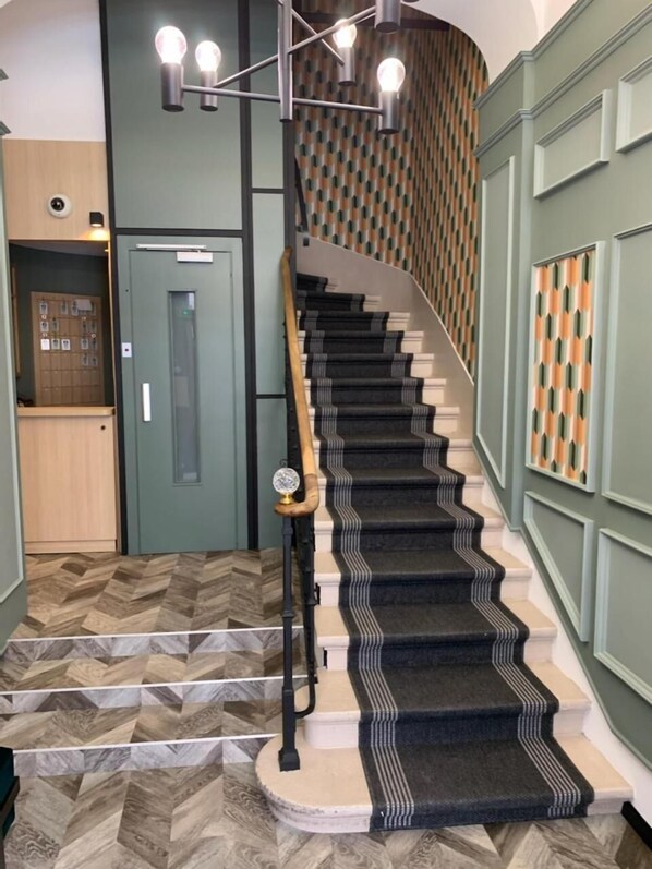 Una escalera con alfombra estampada, barandilla de madera y lámpara moderna.