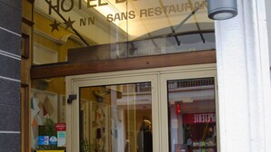 Entrada de un hotel con puerta de cristal, un cartel que dice "HOTEL DU NORI" y un letrero visible de neumáticos Michelin.