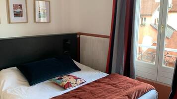 Een hotelkamer met een bed, een radiator en een raam met gordijnen.