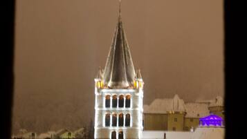A church with a tall spire and illuminated windows, surrounded by buildings and a snowy landscape.