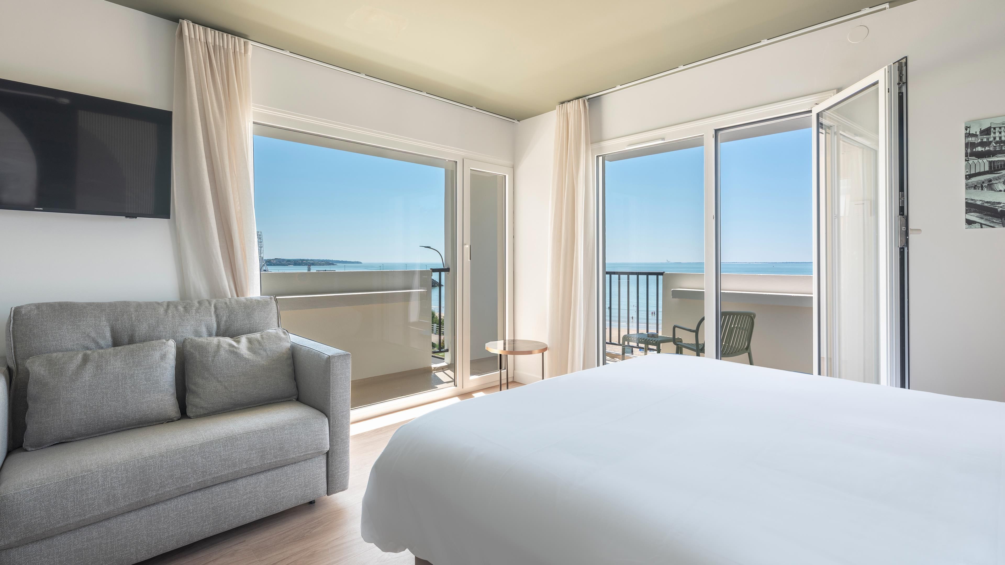 Ein Hotelzimmer mit Bett, Sofa, kleinem Tisch und einem Balkon mit Meerblick.