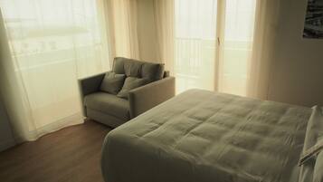 A room with a bed, a chair, and a balcony with curtains.