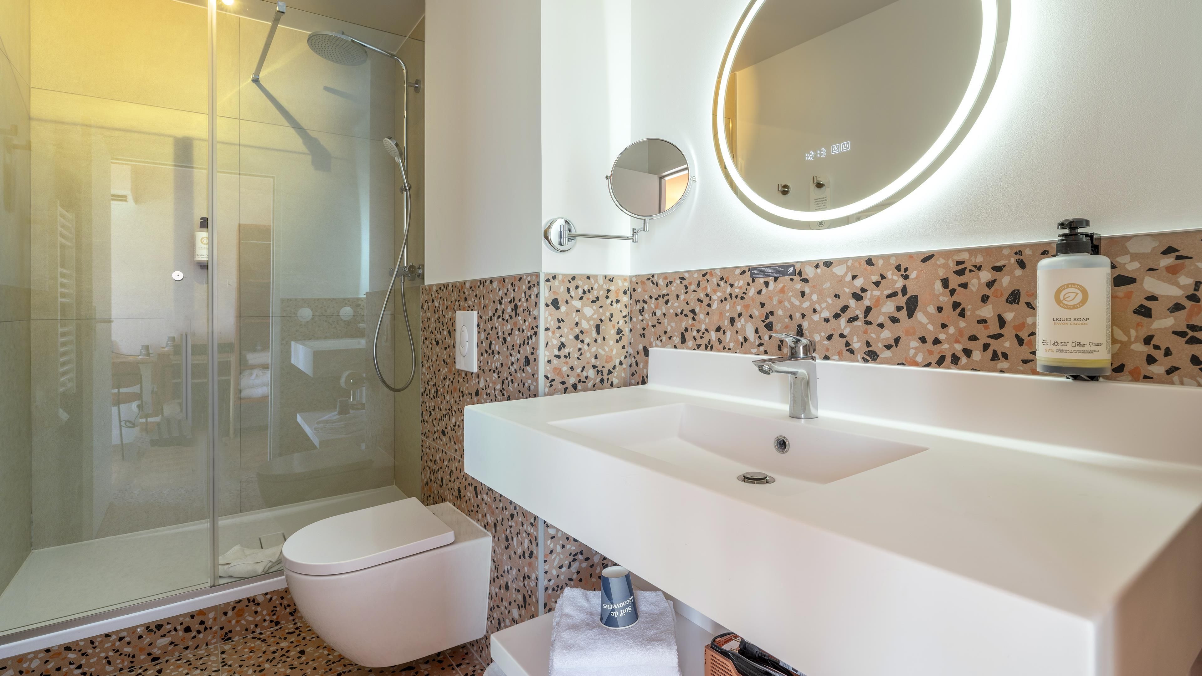 Un baño moderno con ducha envuelta en vidrio, un lavamanos blanco y un espejo redondo.