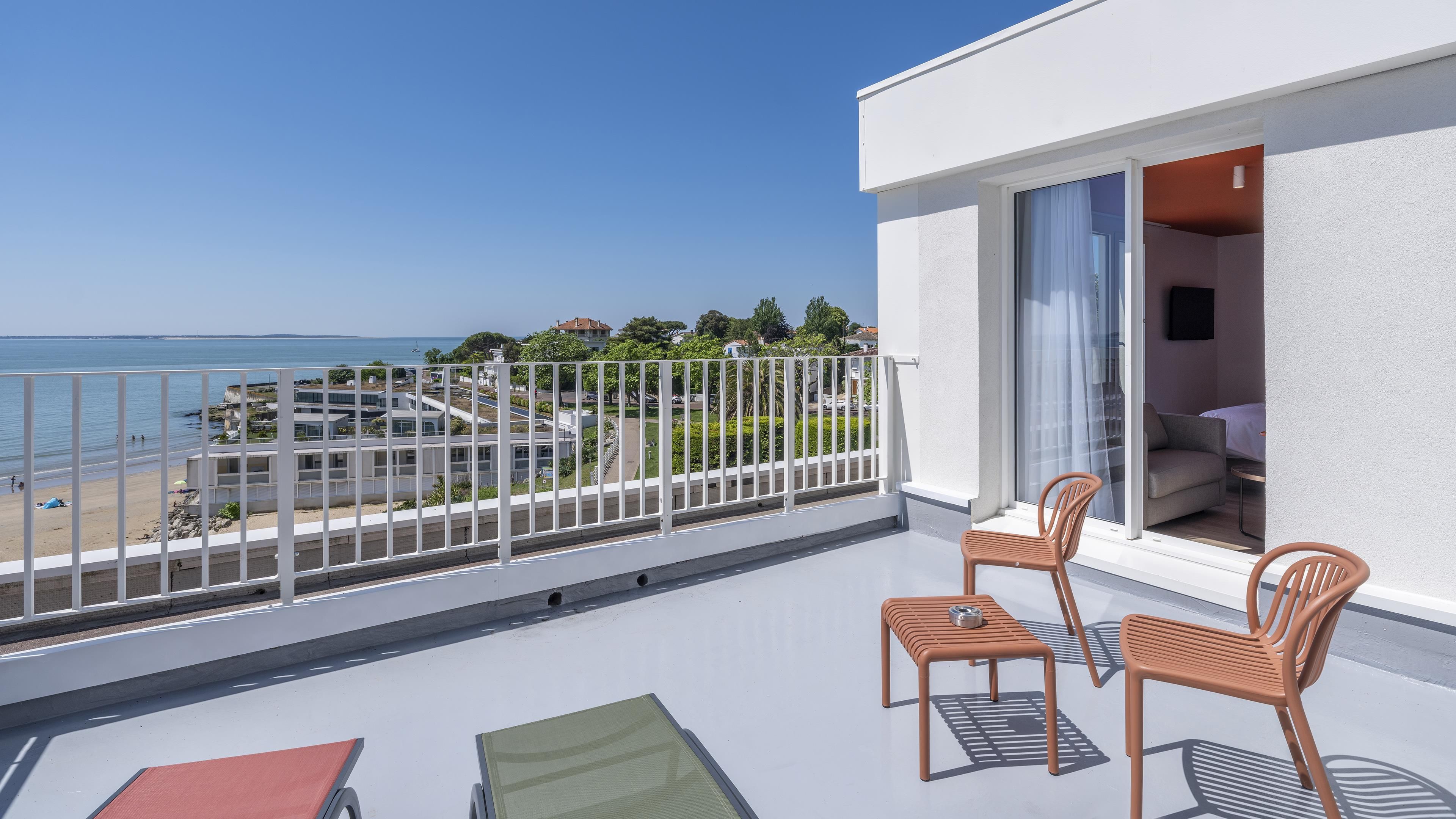 Een balkon met uitzicht op het strand, twee stoelen en een tafel.