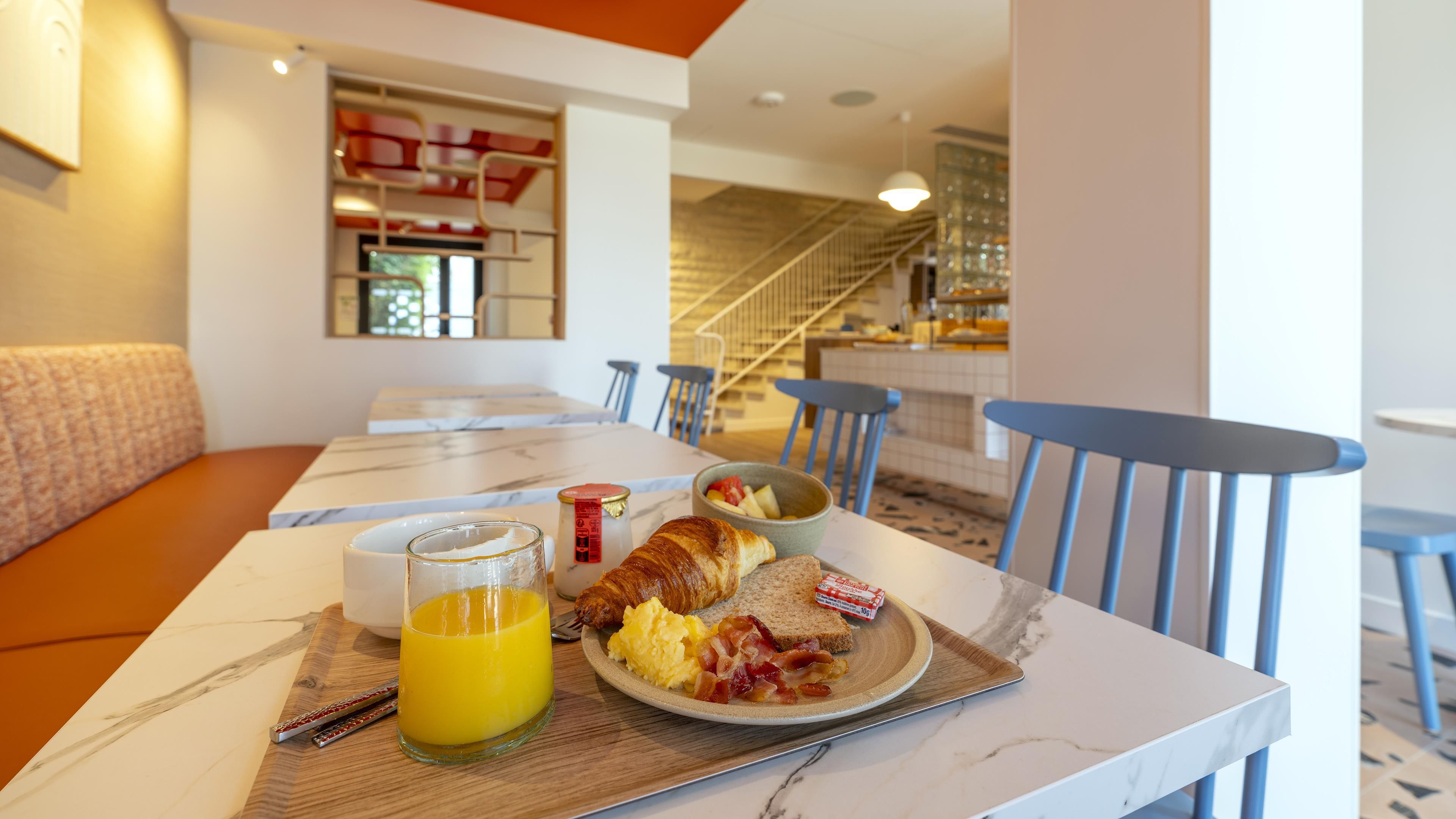 A breakfast table with a croissant, scrambled eggs, bacon, toast, and a bowl of fruit.