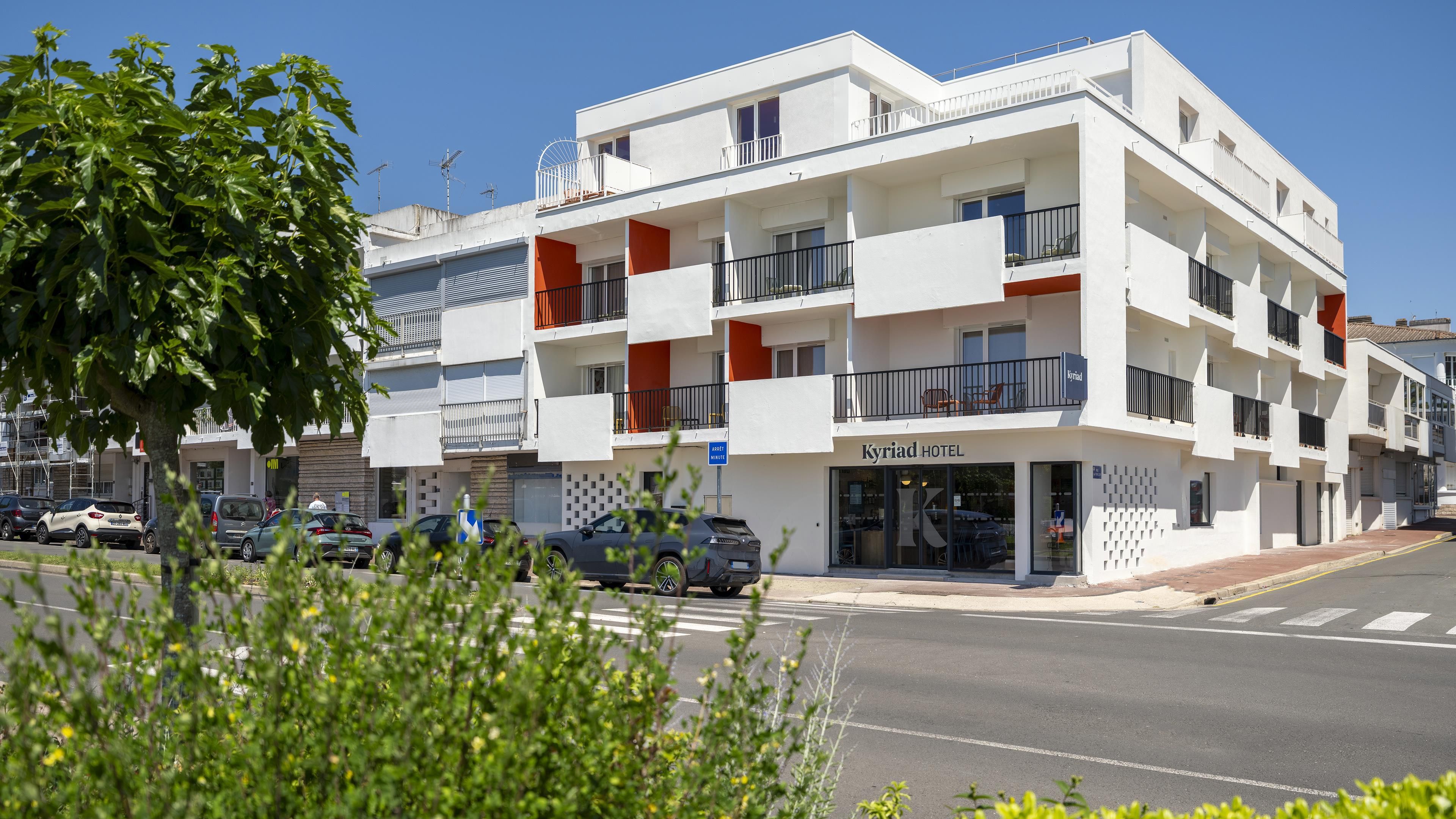 Un hôtel à plusieurs étages doté de balcons, d’une entrée bien visible et d’un espace de stationnement.