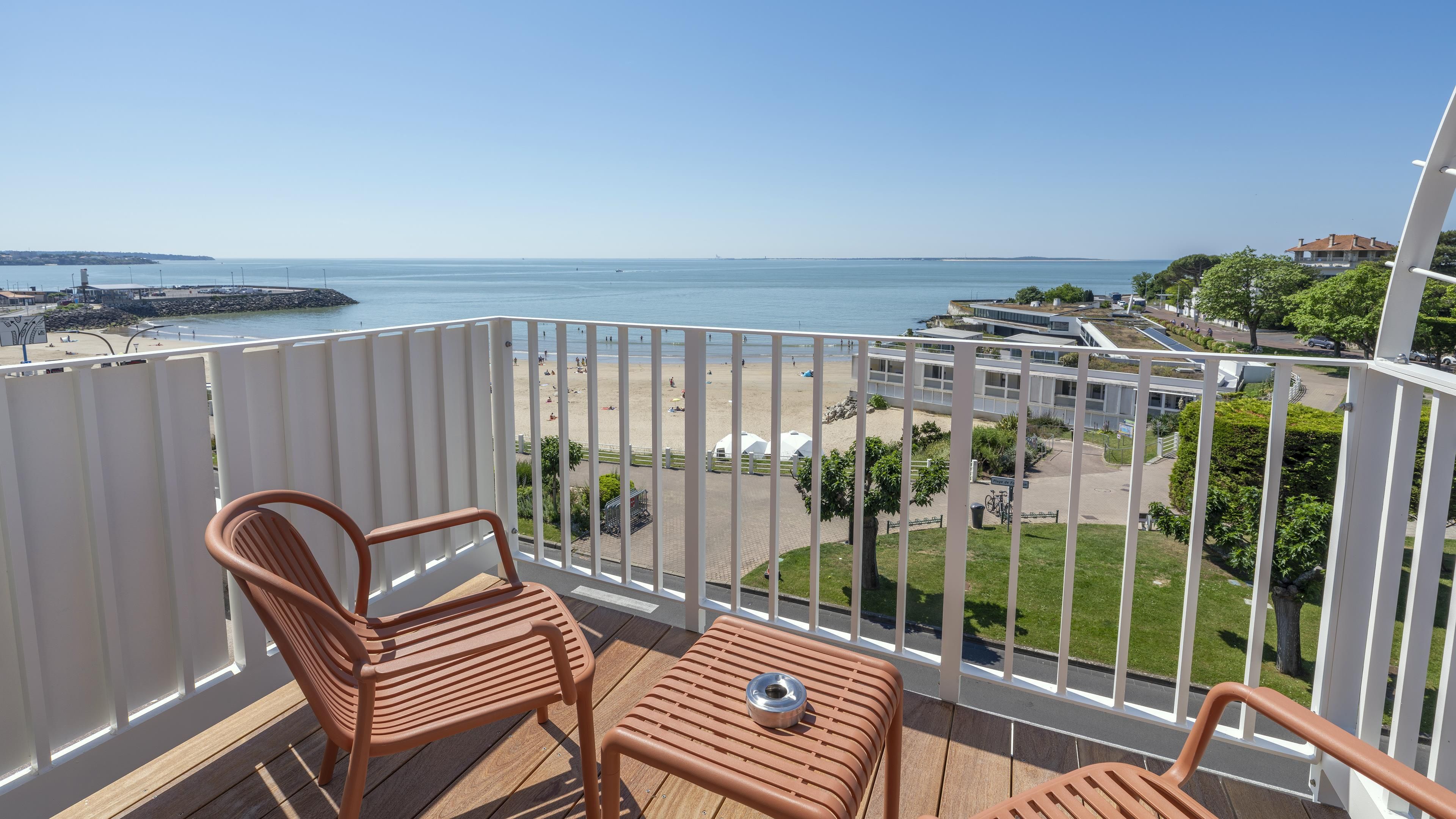 Ein Balkon mit zwei Stühlen und einem kleinen Tisch, der Blick auf einen Strand und eine Küstenstraße bietet.