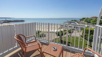 Ein Balkon mit zwei Stühlen und einem kleinen Tisch, der Blick auf einen Strand und eine Küstenstraße bietet.
