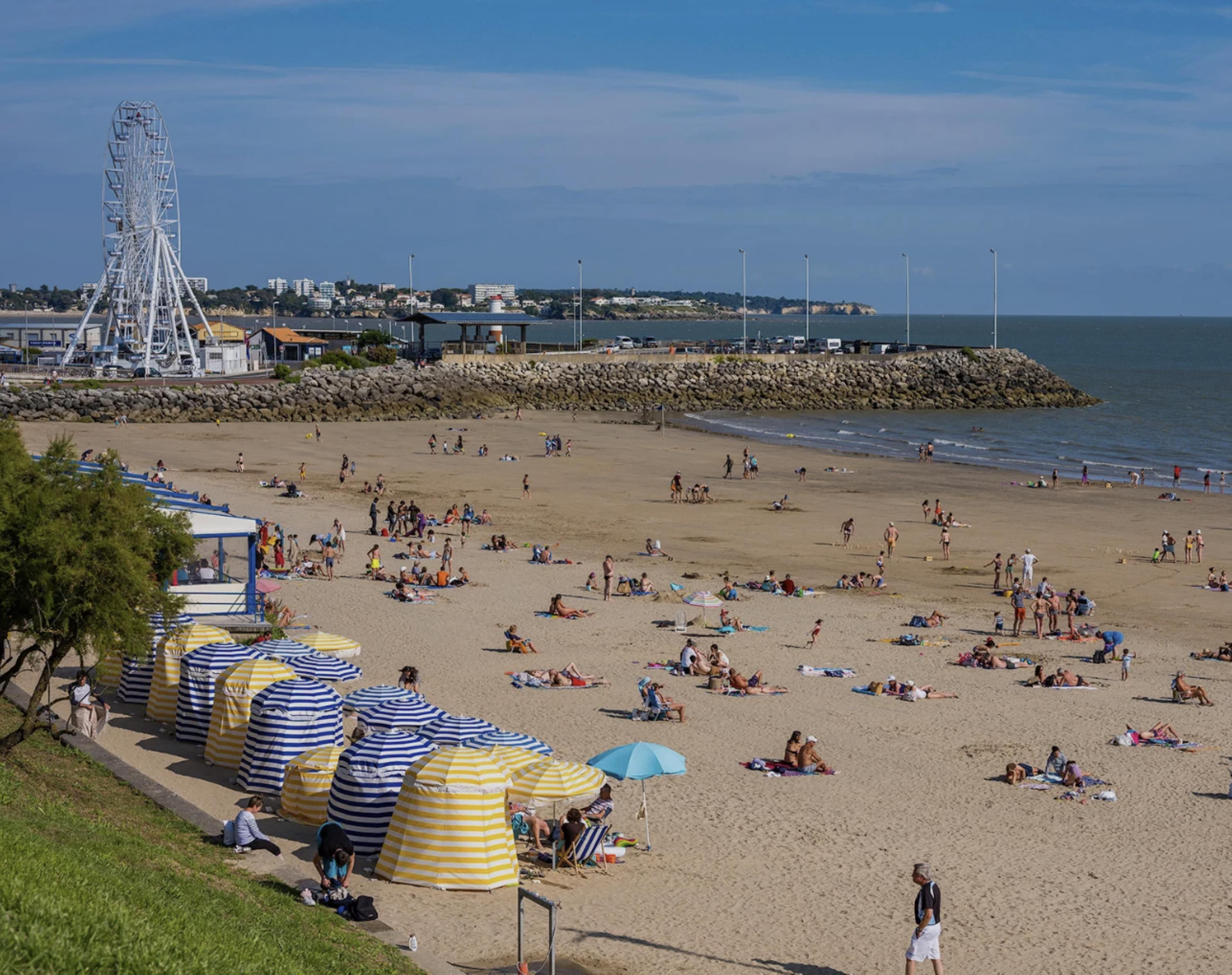 Ein Strand mit Sonnenschirmen, einem Riesenrad und einer felsigen Küstenlinie.