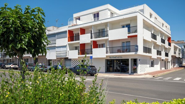 A multi-story hotel with balconies, a visible entrance, and parked cars.