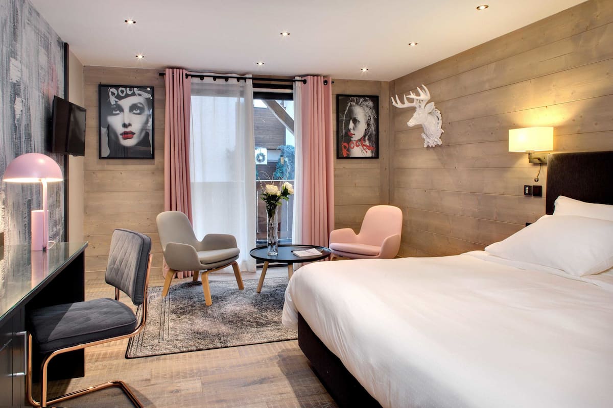 Una habitación de hotel moderna con una cama grande, dos sillones, un escritorio y un televisor.