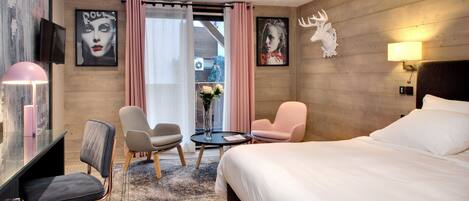 A modern hotel room with a large bed, two armchairs, a desk, and a TV.