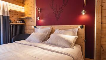 A wooden room with a bed, a red wall with a deer head mural, and two wall-mounted lights.