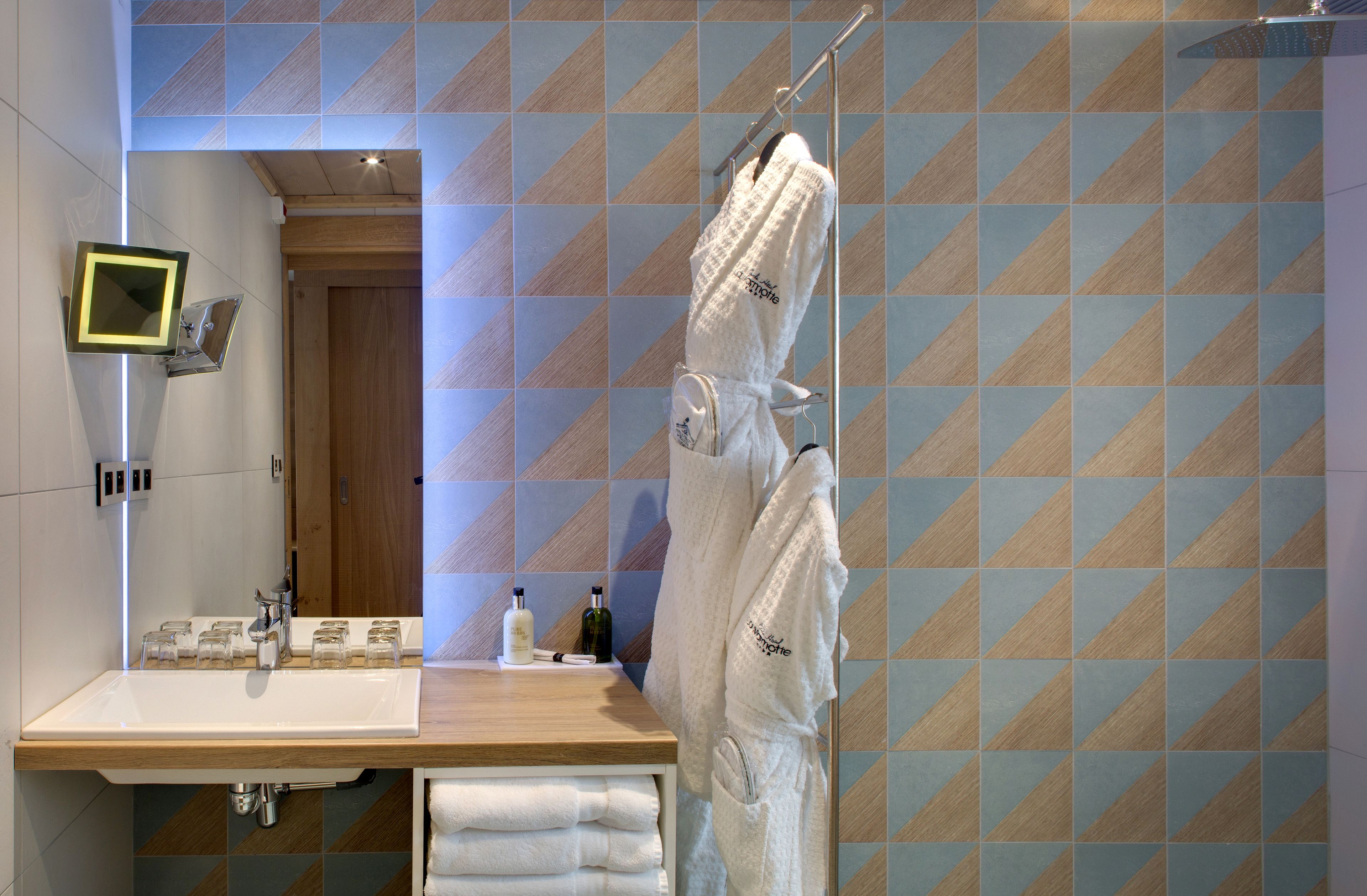 A bathroom with a wooden vanity, a mirror, a towel rack, and a patterned wall.