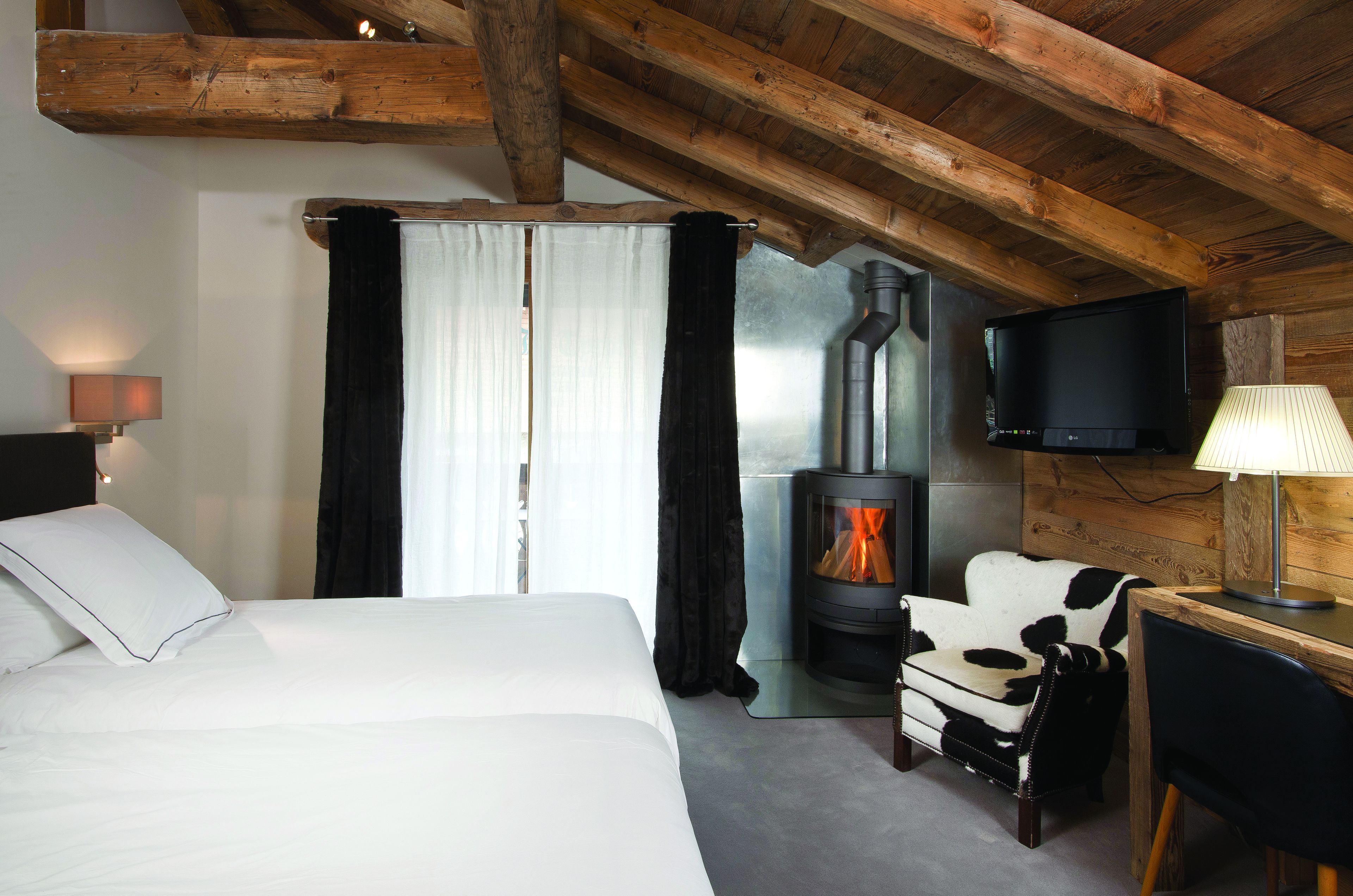 A hotel room with a bed, a sofa, a TV, a fireplace, and a desk.