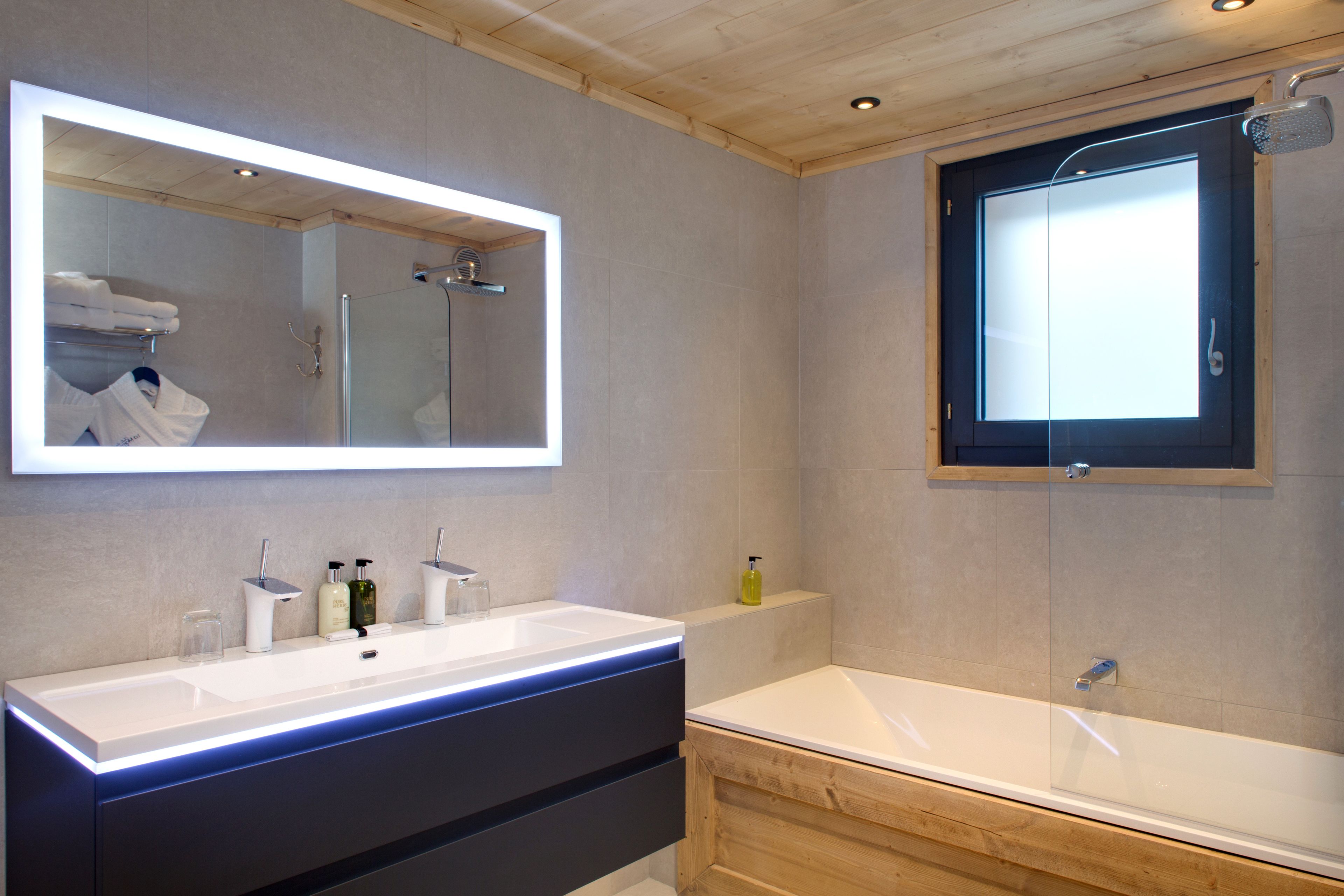 Un baño moderno con un espejo grande, un tocador doble, una bañera y una ducha.