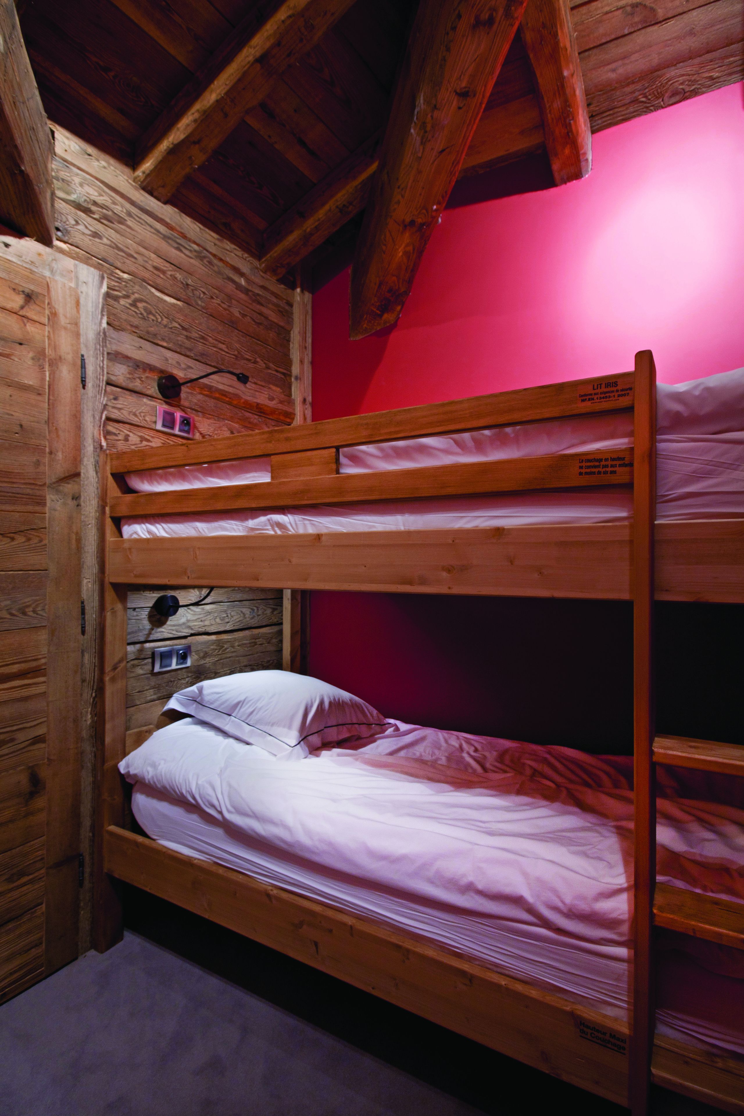 A bunk bed room with wooden walls and a red wall behind the upper bunk.