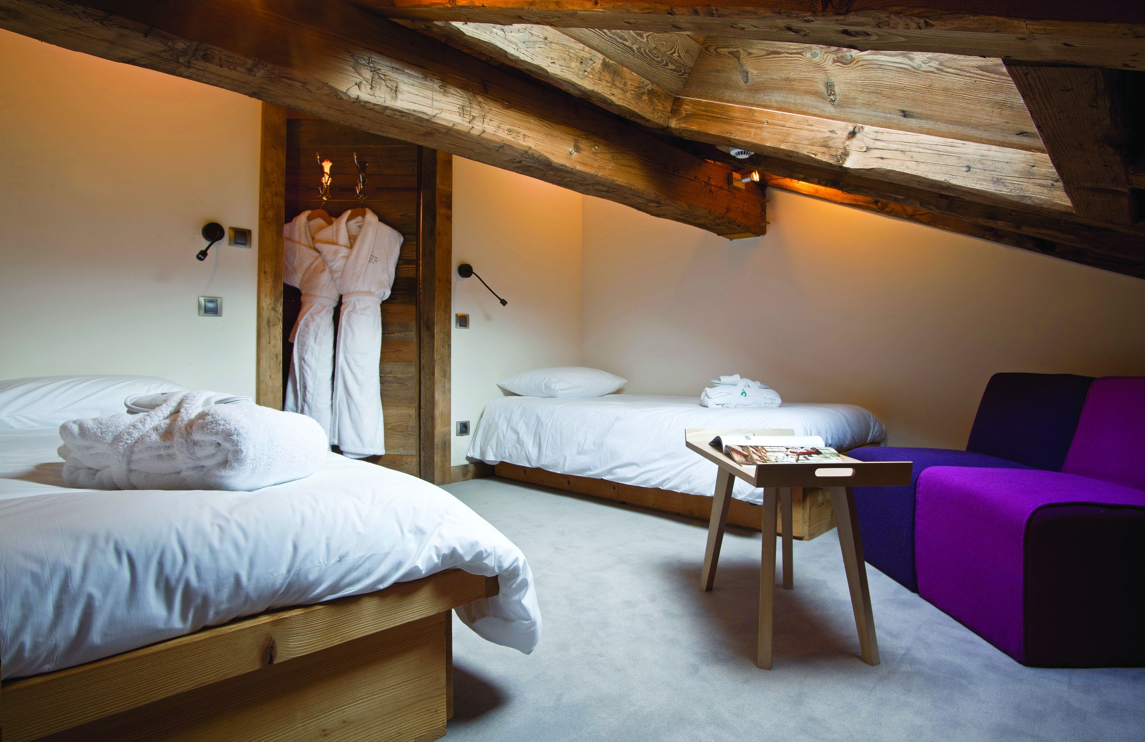 A room with two beds, a wooden table, a purple sofa, and a robe hanging on the wall.