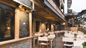 An outdoor dining area with wooden tables and chairs, a chalkboard menu, and a sign reading "LA PIVOTIT".