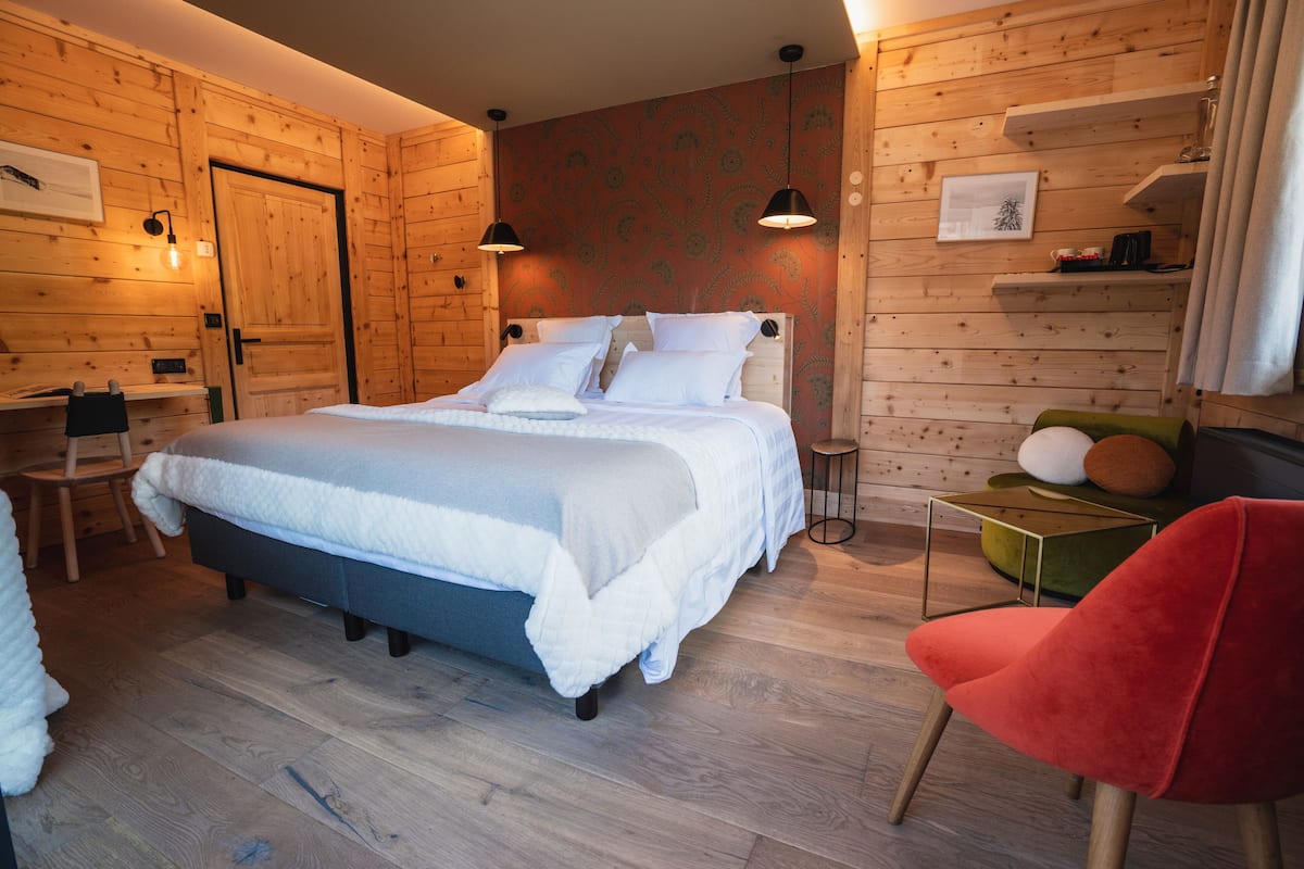 Un dormitorio con paneles de madera, una cama, mesitas de noche y una silla roja.