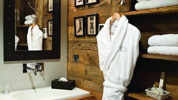 A bathroom with a wooden wall, a large mirror, a white sink, and a towel rack with a white bathrobe hanging.
