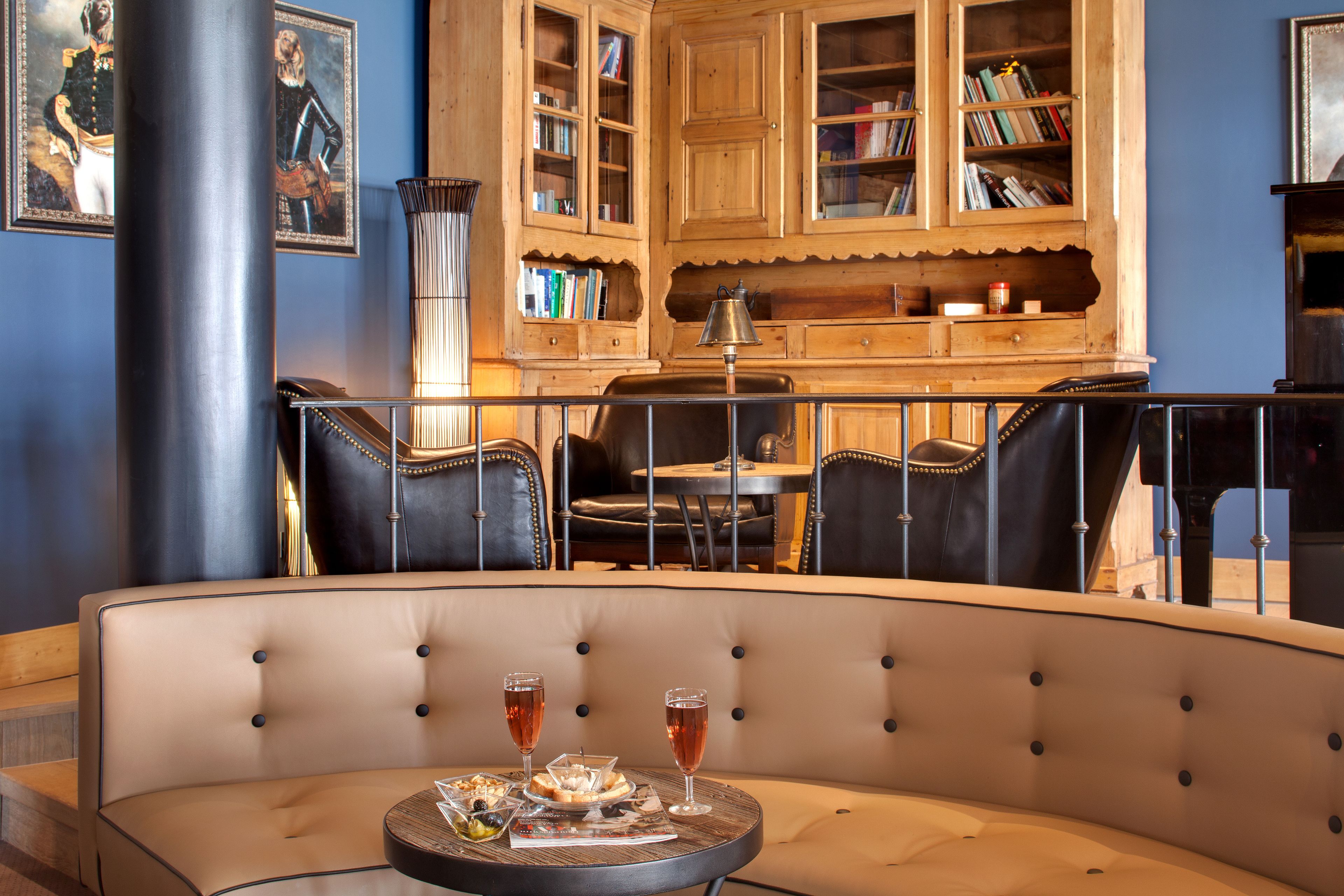 A dining area with a round table, two chairs, and a bar stool. There are two glasses of a pink beverage on the table.