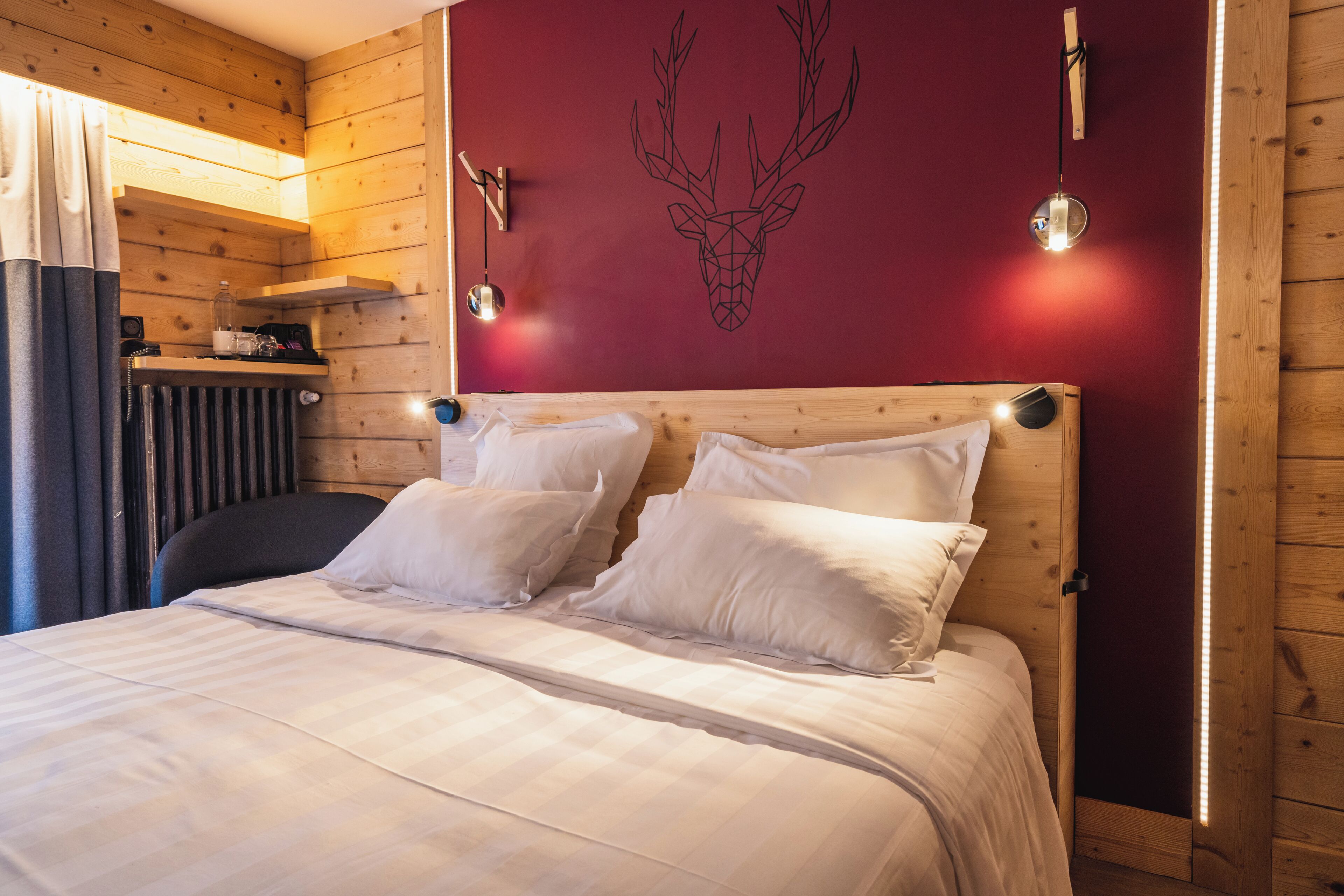 Una habitación tipo cabaña de madera con una cama, una lámpara fijada a la pared y una decoración de cabeza de ciervo.