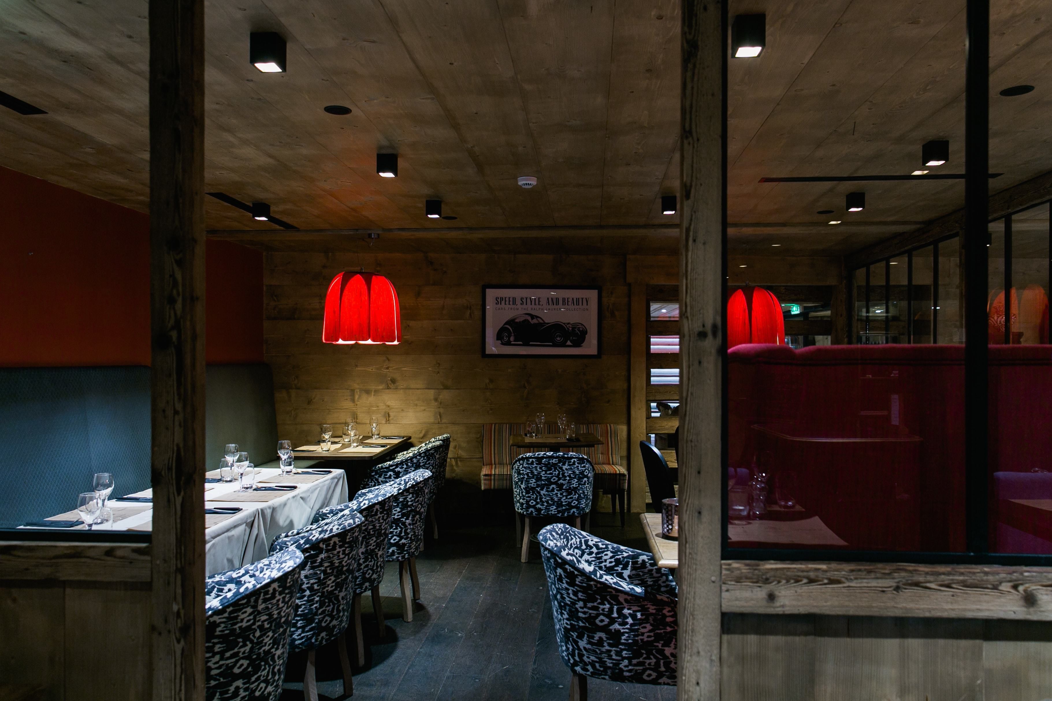 Interior de restaurante con paredes de madera, sillas estampadas y lámparas colgantes rojas.