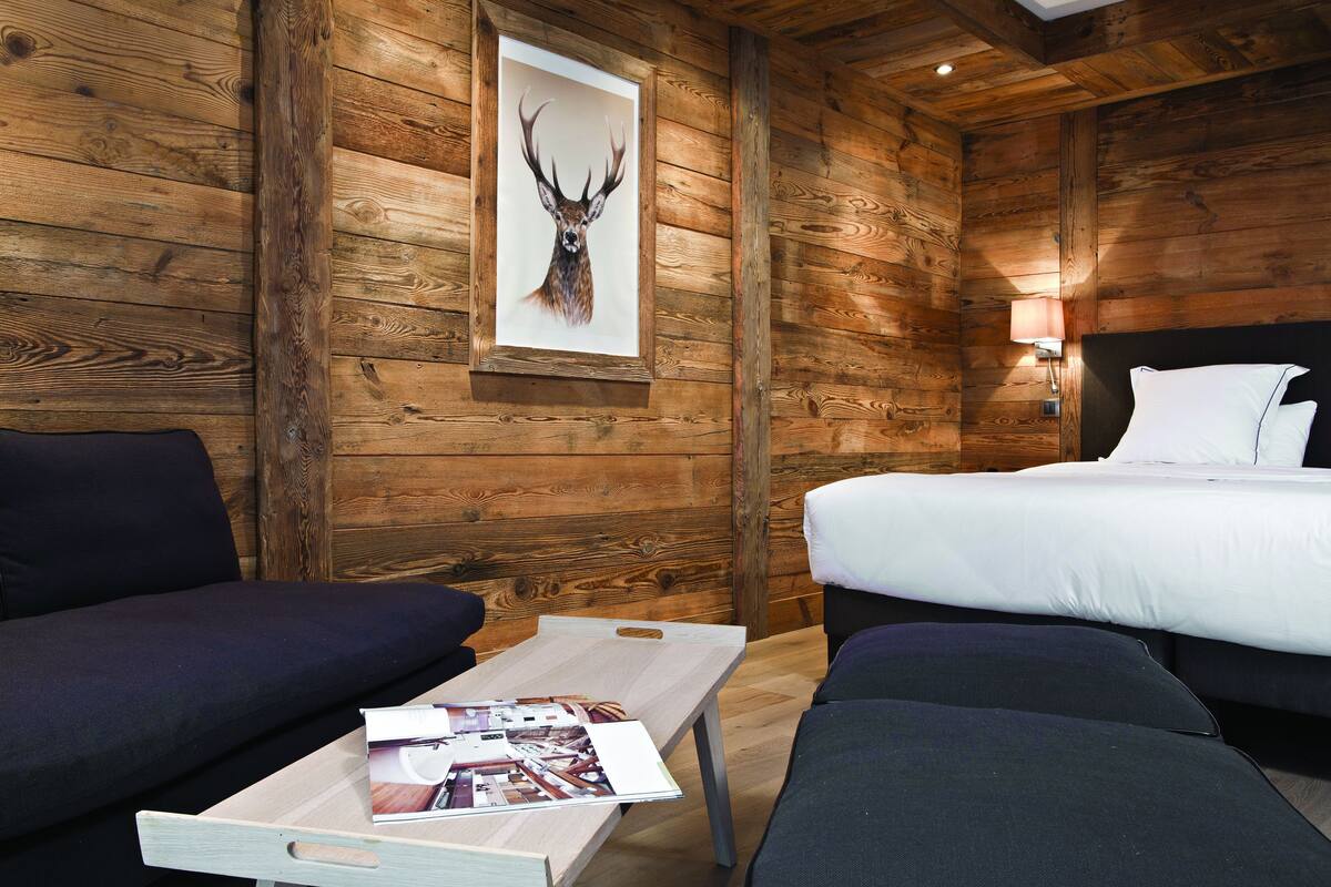 Una habitación tipo cabaña de madera con una cama, dos sofás y una mesa con una revista.