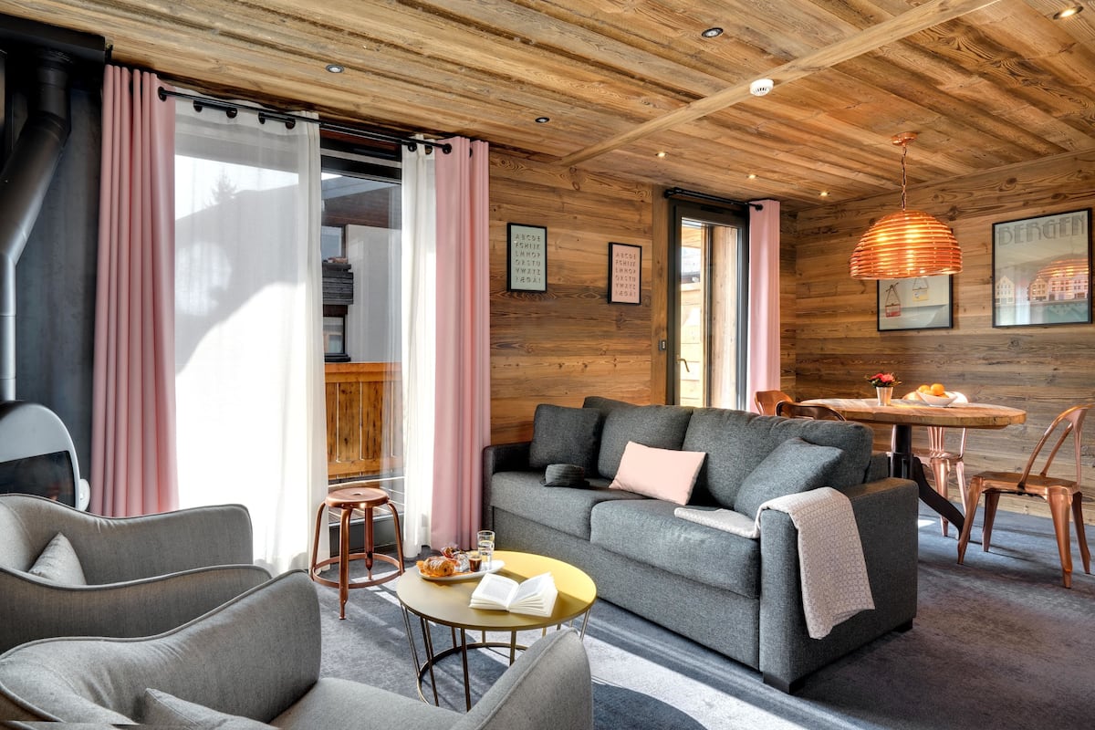 Un salón acogedor con un sofá gris, dos sillones, una mesa redonda de centro y techo de madera.