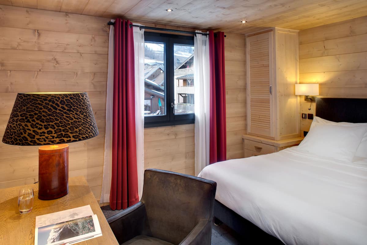 Una habitación de hotel con una cama, una silla, una mesa con lámpara y una ventana con cortinas.