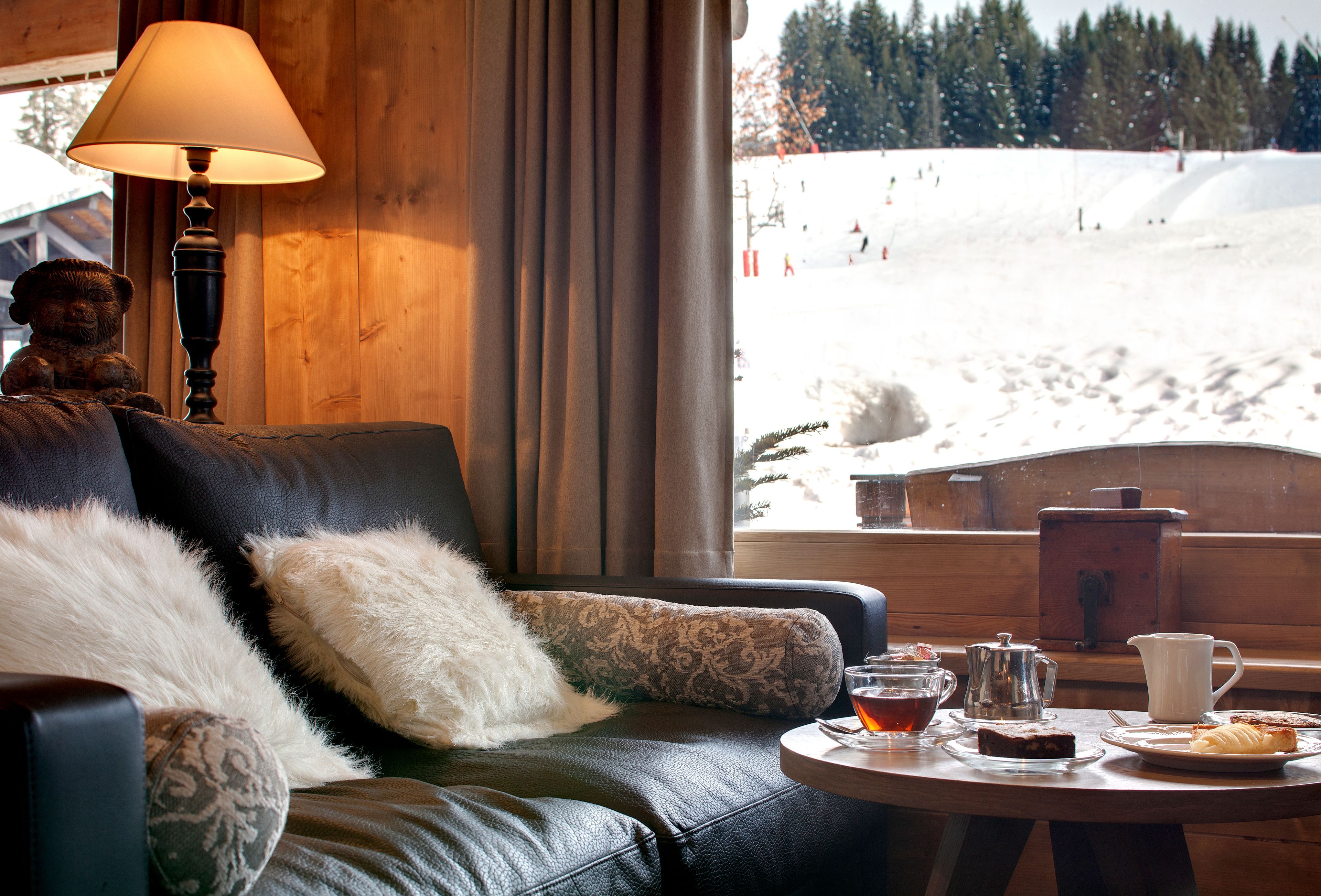A cozy room with a leather sofa, a lamp, a table with a teapot, a cup, and a plate with a pastry.