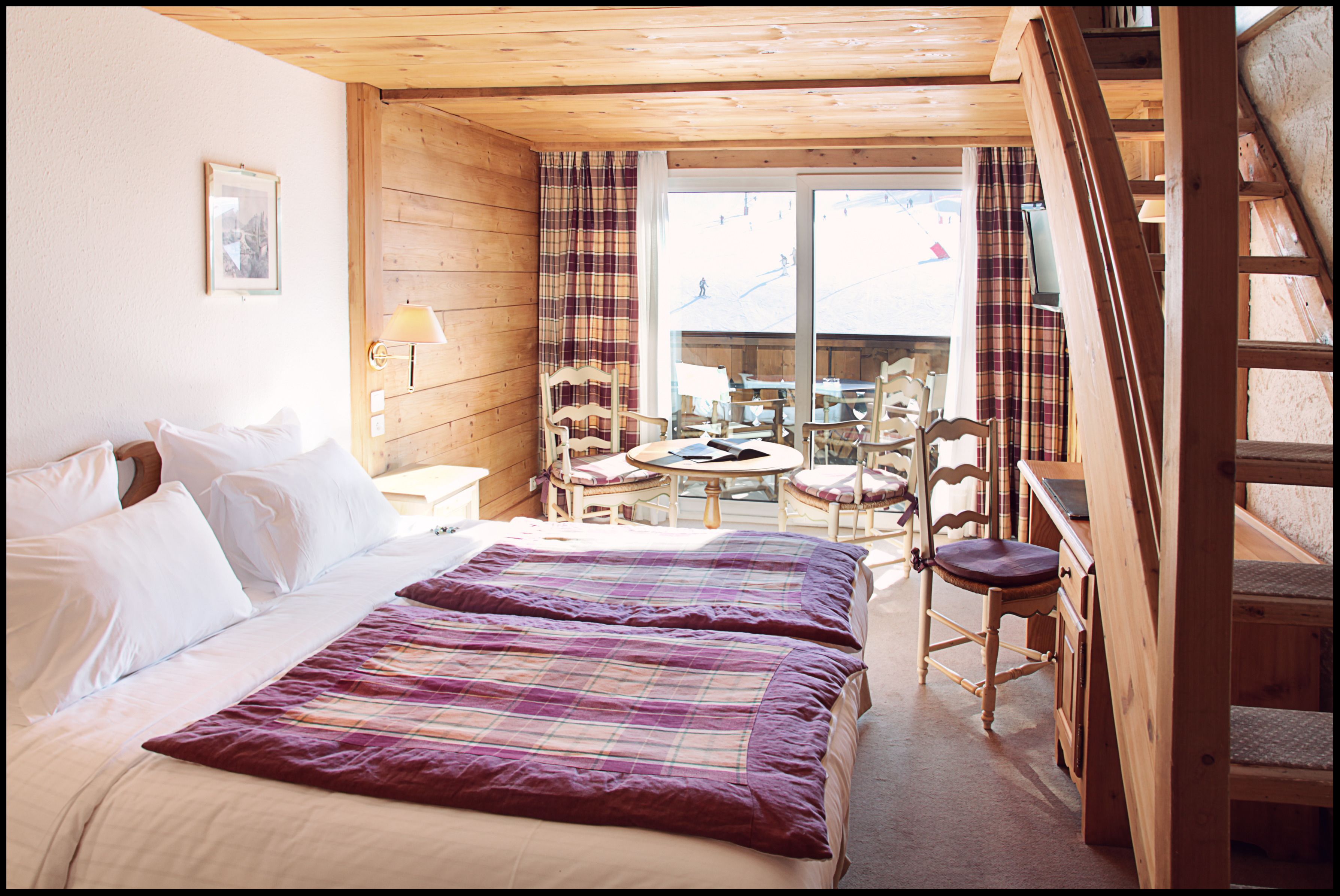 Een houten kamer met een bed, twee stoelen, een tafel en een televisie.