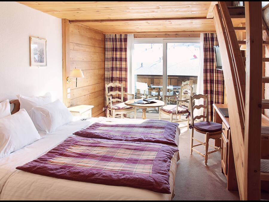 A wooden cabin room with a bed, two chairs, a table, and a TV.