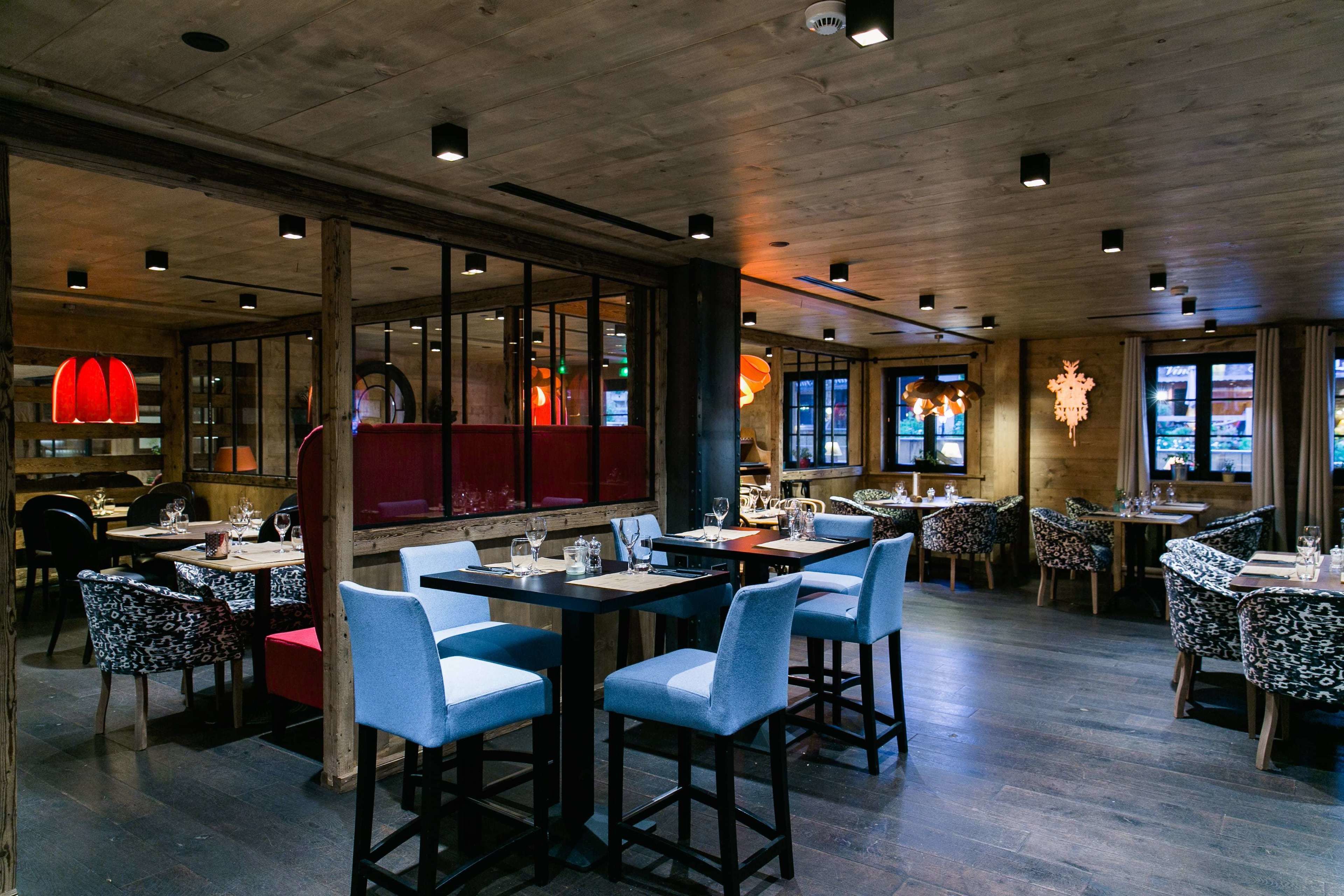 A restaurant with wooden ceiling and walls, tables with blue chairs, and red seating.