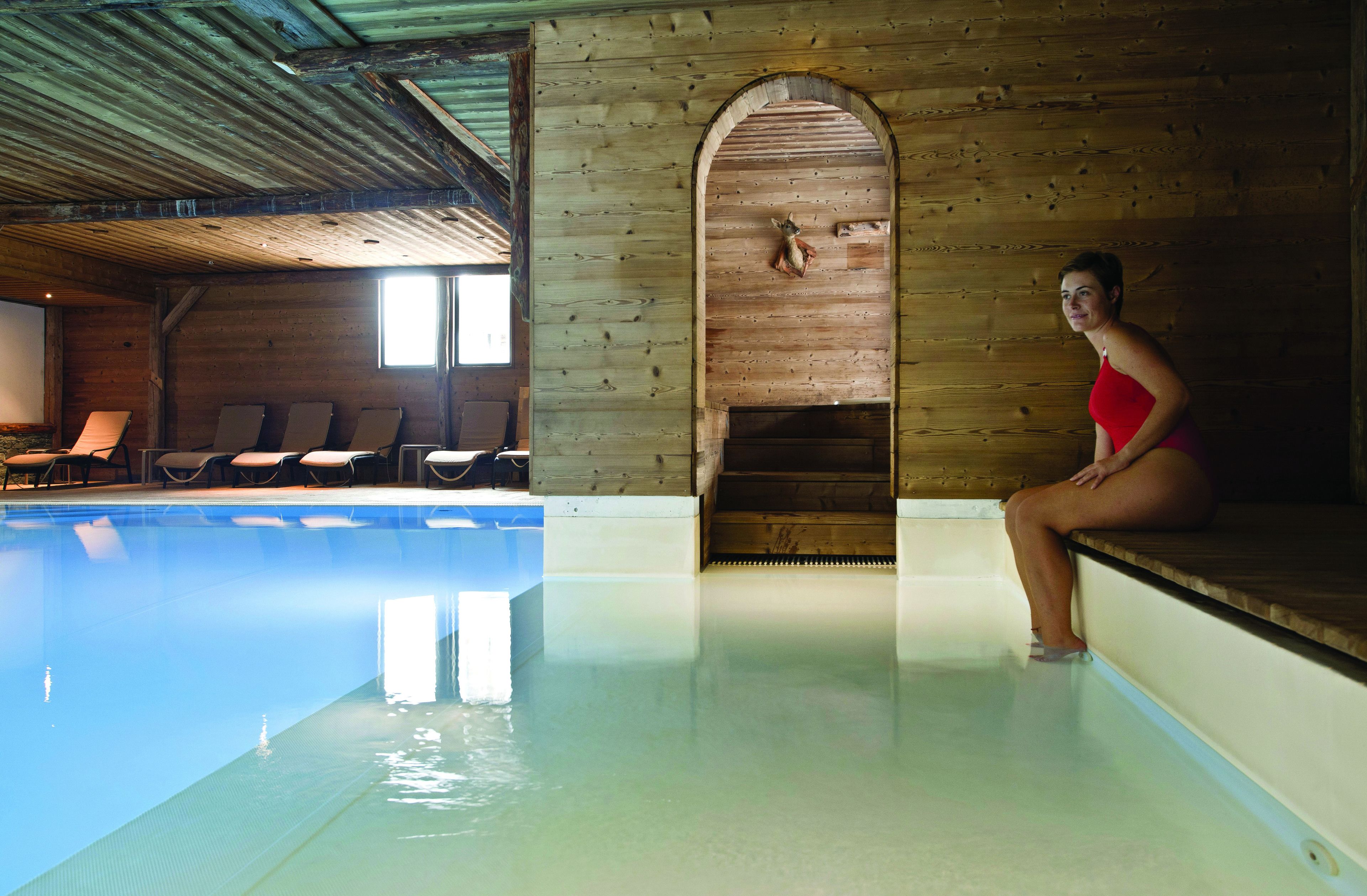 A swimming pool with clear water, wooden walls, and a woman sitting on the edge.