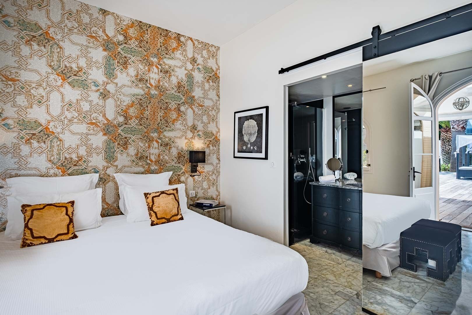 Een hotelkamer met een groot bed, een badkamer met spiegel en toiletartikelen, en uitzicht door een open deur.