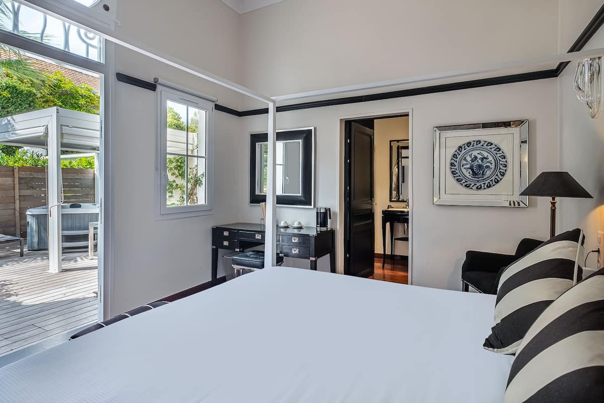 A bedroom with a large bed, a desk with a mirror, a framed picture on the wall, and a view of the outdoors through a sliding door.