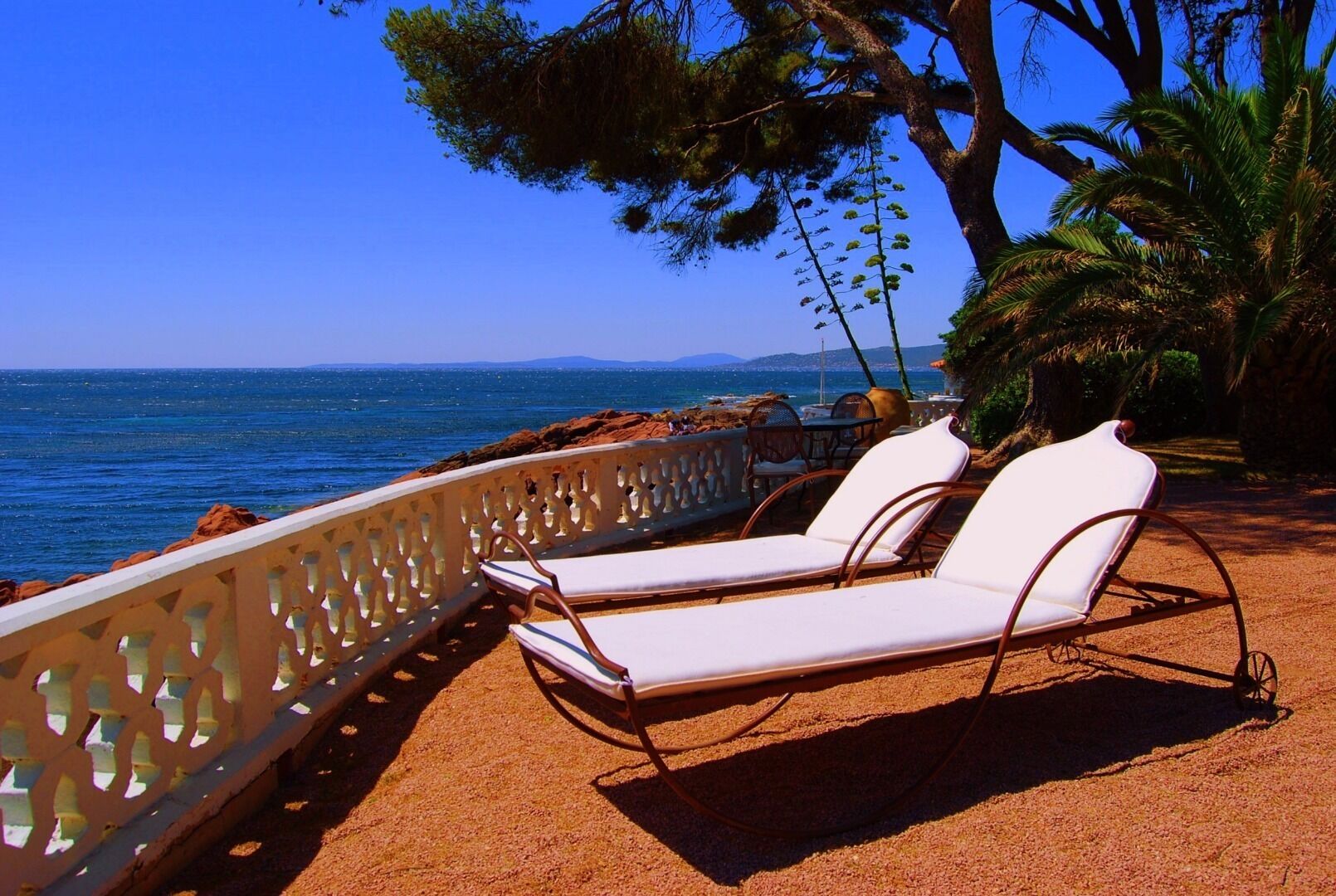 A beachside lounge with white cushioned chairs and a decorative railing overlooking the sea.