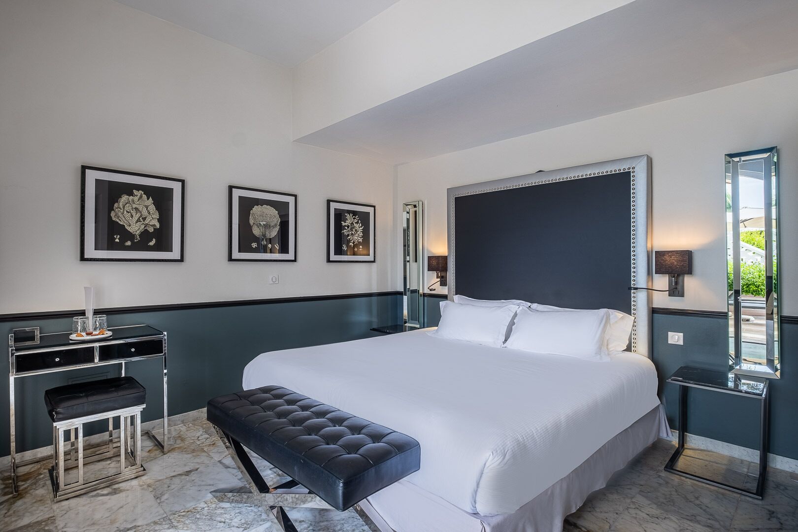 Moderni hotellihuone, jossa on suuri sänky, yöpöytä, penkki ja seinällä kehystetty taideteos.