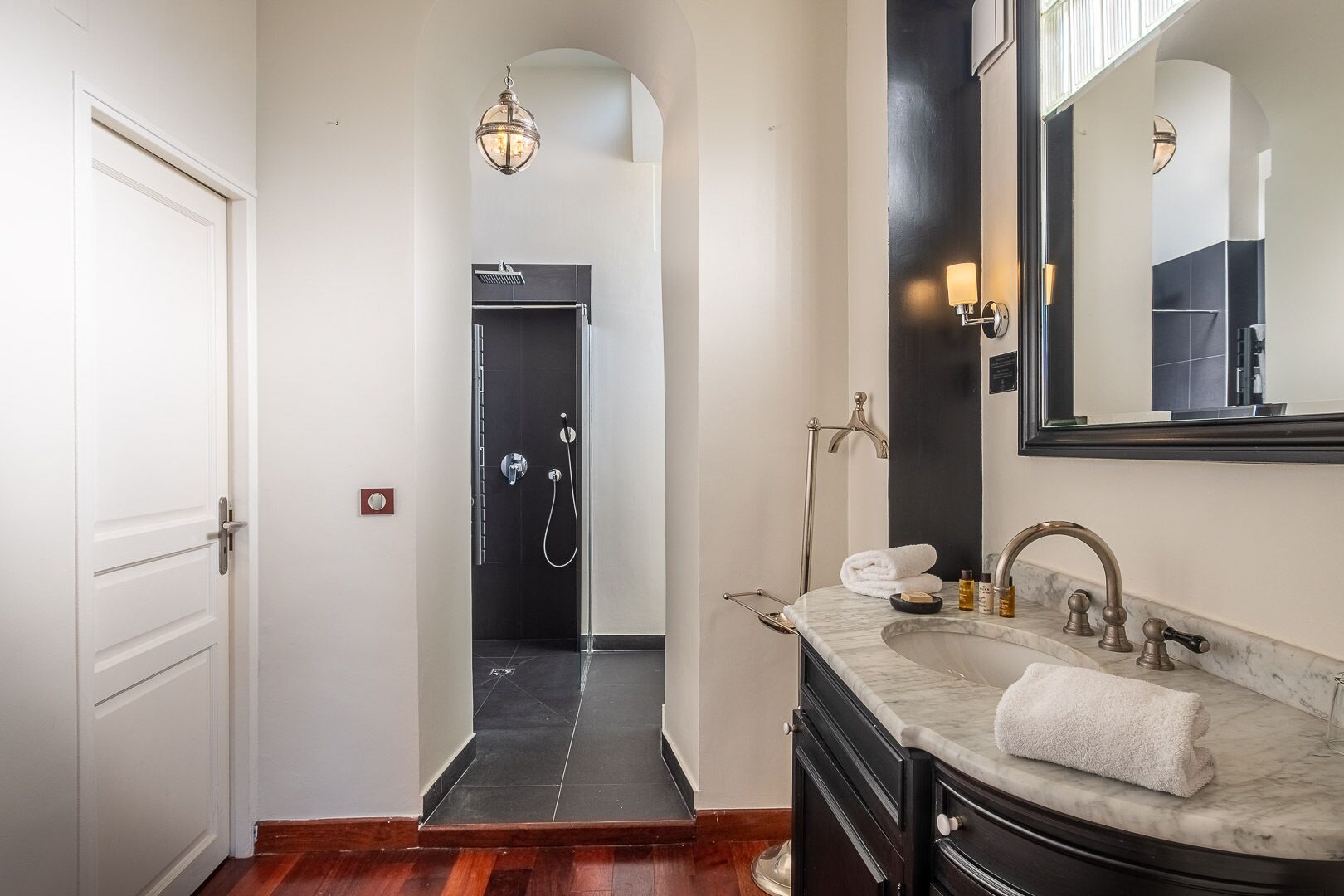 Un baño moderno con lavamanos de mármol, un espejo grande y una zona de ducha.