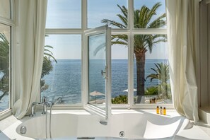A bathroom with a large window offering a view of the sea and palm trees. - La Villa Mauresque (Saint-Raphael)