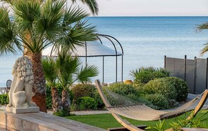 Un hamac, une statue de lion en pierre et un palmier au bord d’une piscine, avec vue sur la mer.