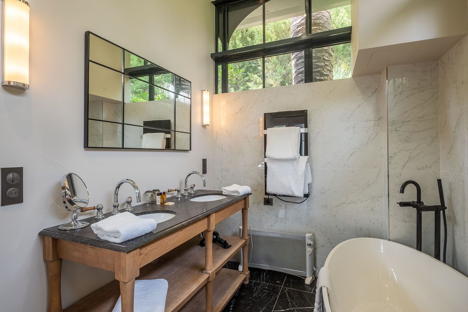 Un baño con dos lavamanos, un espejo grande, un perchero para toallas, una ducha y una bañera.