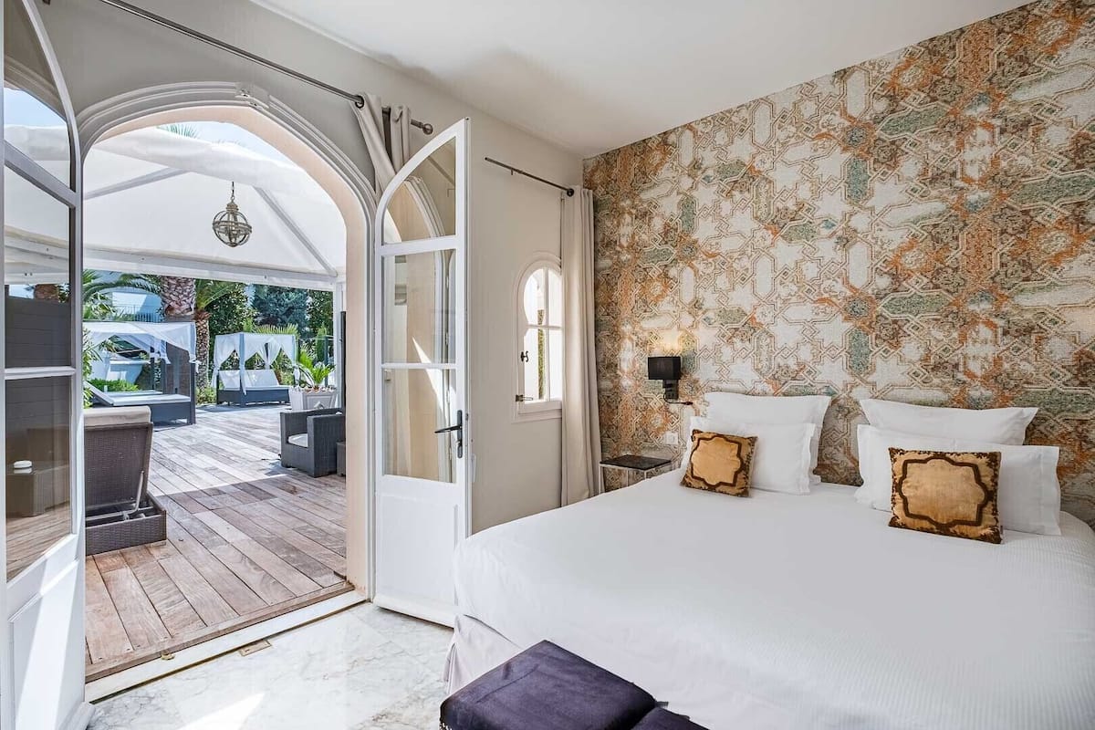 A bedroom with a large bed, a view of an outdoor deck, and a patterned wall.