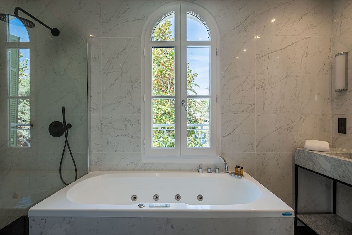 A modern bathroom with a large freestanding bathtub, a walk-in shower, and a window with a view of greenery.